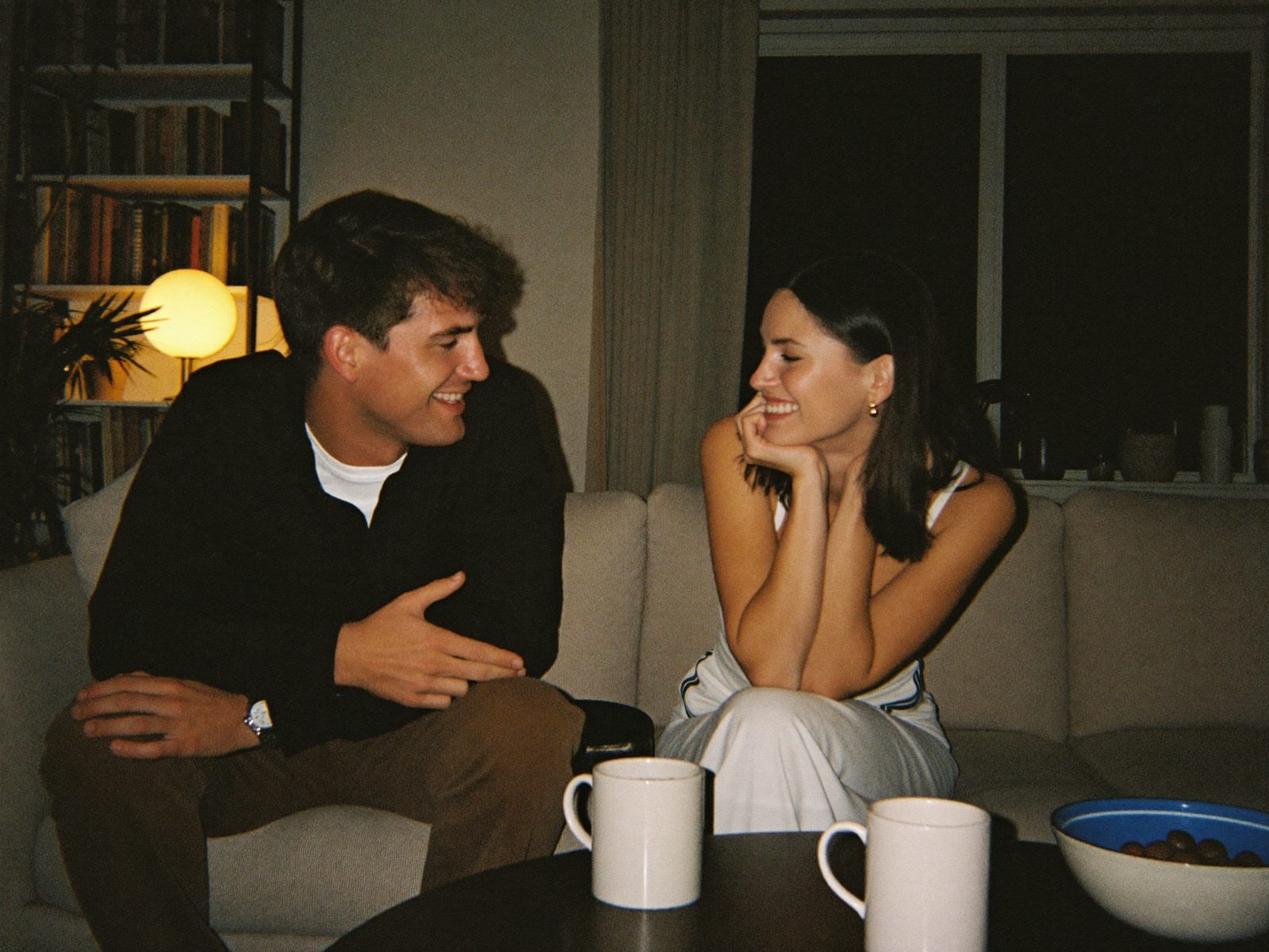 Two people deep in conversation on a sofa, lit by warm lamp light