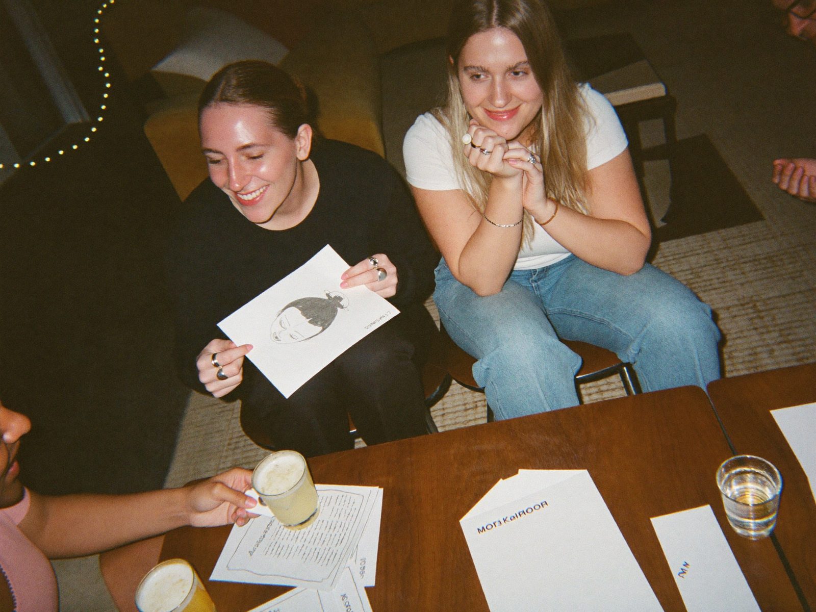 Four people around a coffee table laughing as one holds up a hand-drawn sketch
